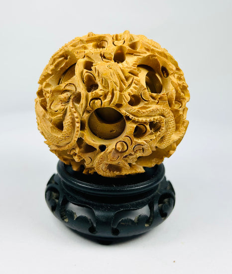 Chinese antique puzzle ball with detailed dragon and cloud carvings on a black carved stand against a white background.