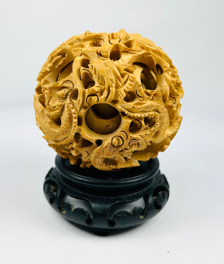 Chinese antique puzzle ball with detailed dragon and cloud carvings on a black carved stand against a white background.
