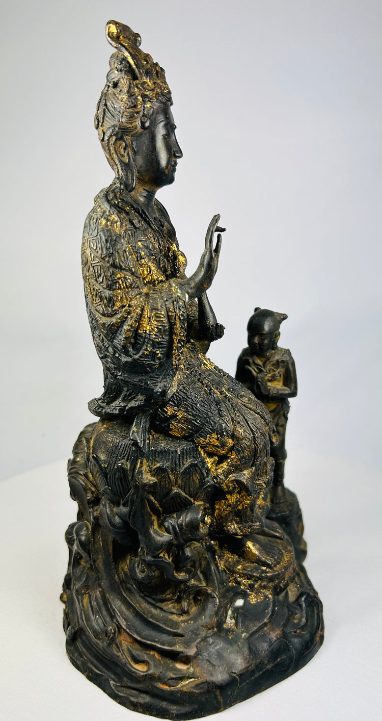 Left-side angle of antique Thai bronze Guanyin statue showing robe folds, lotus petals, and aged patina.