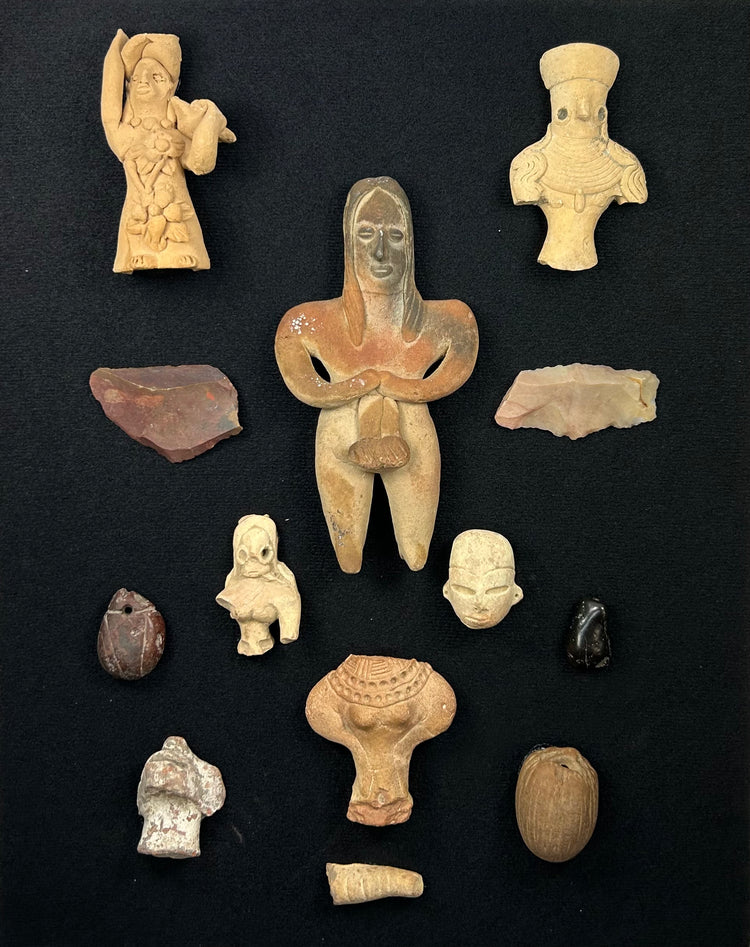Pre-Columbian terracotta figurines, stone blades, and amulets arranged on a black display background.