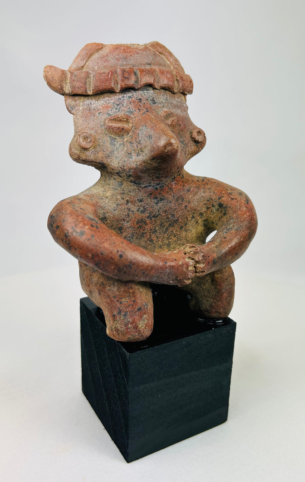 Ancient West Mexico terracotta figure seated with hands clasped, frontal view.