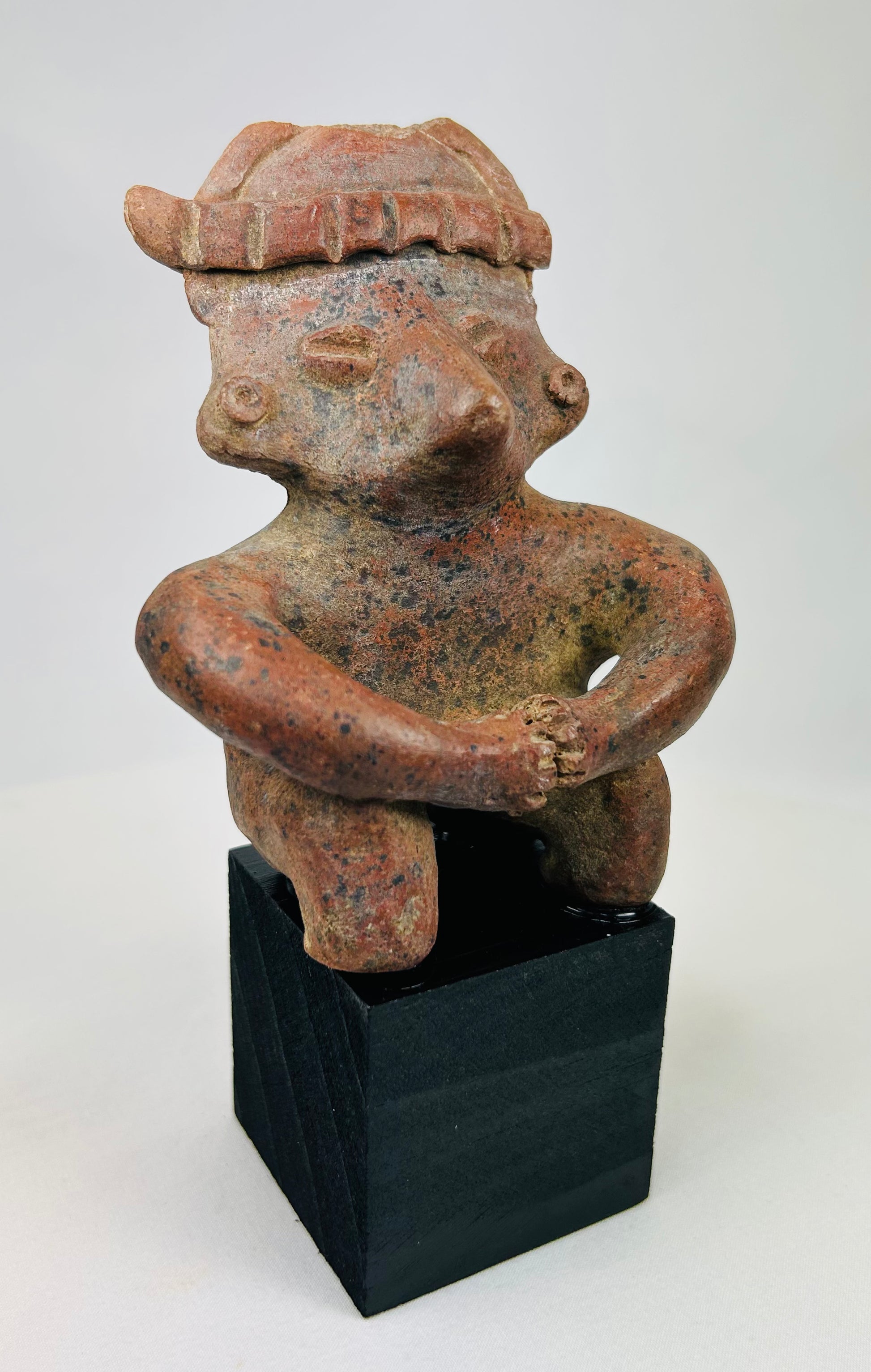 Ancient West Mexico terracotta figure seated with hands clasped, frontal view.