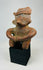 Ancient Nayarit figurine with rounded body and headdress on museum display stand.