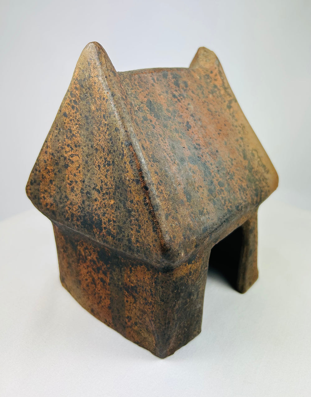 Angled photograph of ancient clay house model with textured sloping roof.