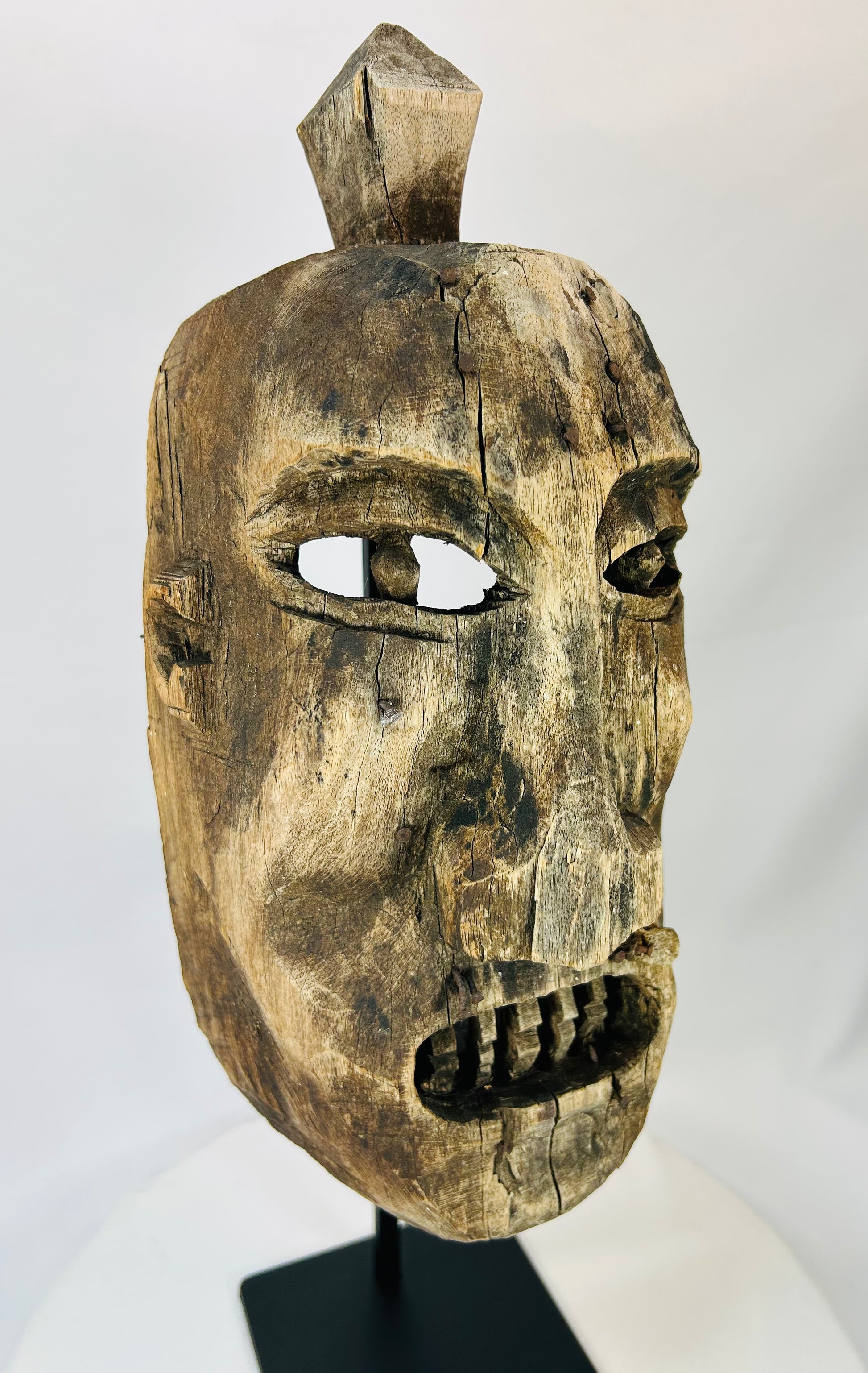 Side profile of a carved wooden ritual mask showing deep patina and sculpted facial contours.