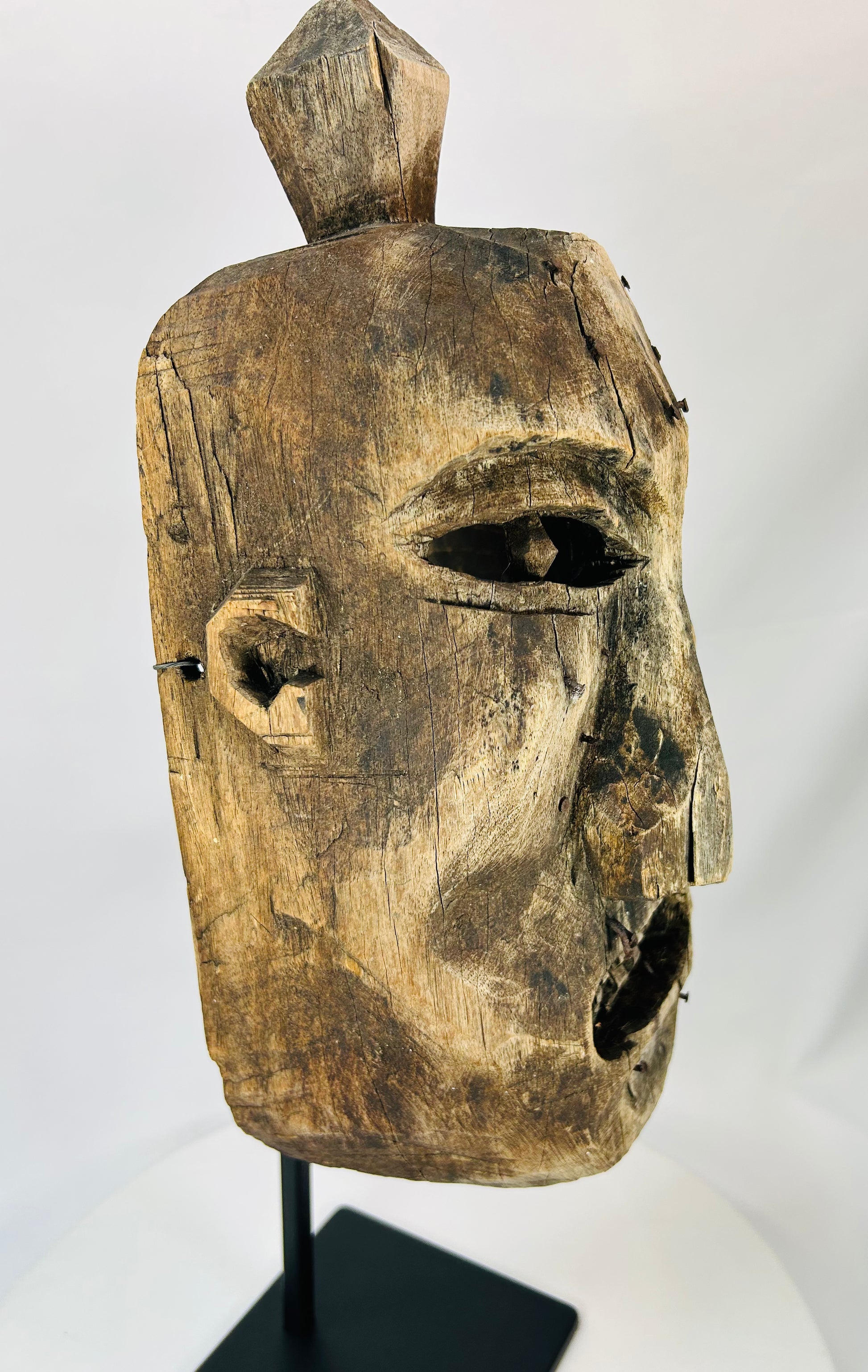 Angled view of an antique tribal-style wooden mask highlighting the weathered texture.