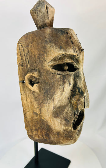 Angled view of an antique tribal-style wooden mask highlighting the weathered texture.