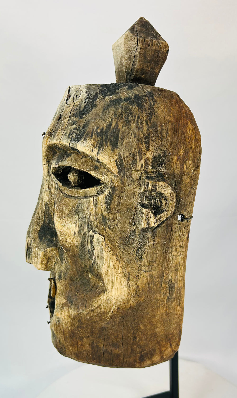 Oblique angle of a carved wooden mask revealing surface cracking and age wear.