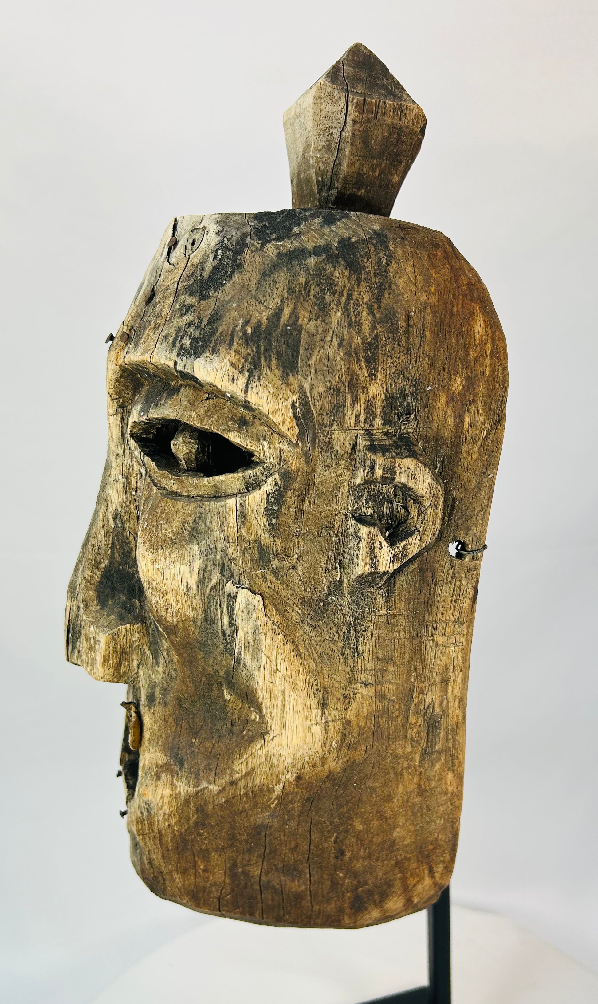 Oblique angle of a carved wooden mask revealing surface cracking and age wear.