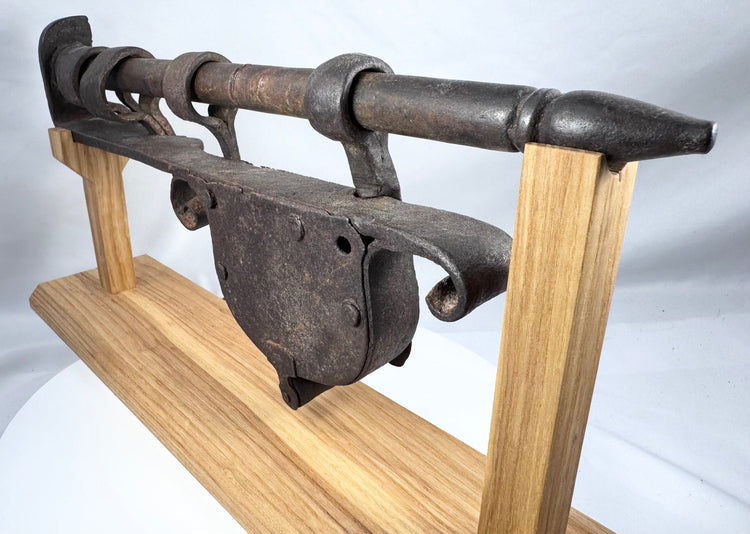 Rear angle of a large hand-forged gate lock mounted on a custom wooden stand