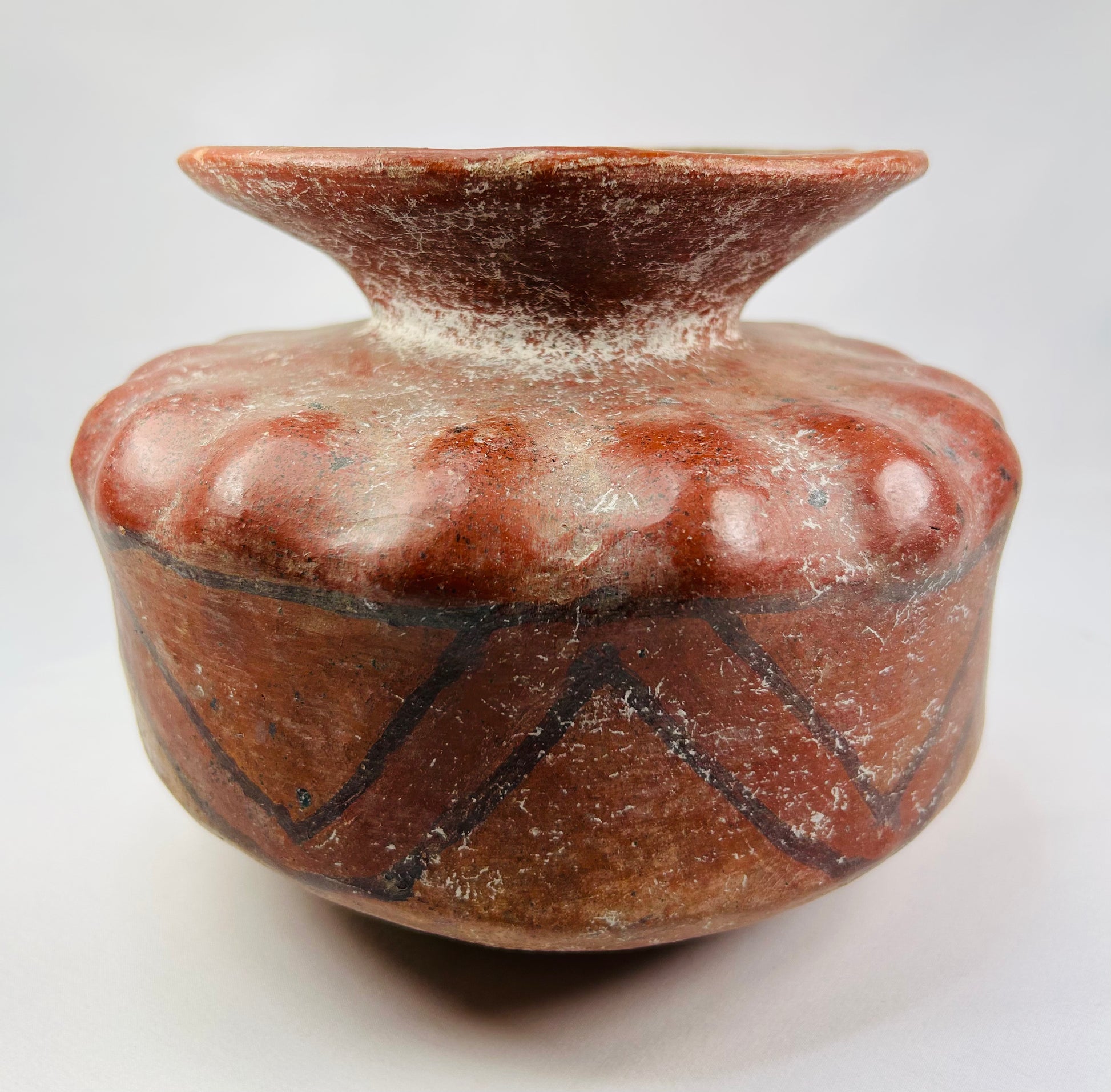 Side view of a Pre-Columbian terracotta vessel with zig-zag geometric paint and scalloped shoulder.