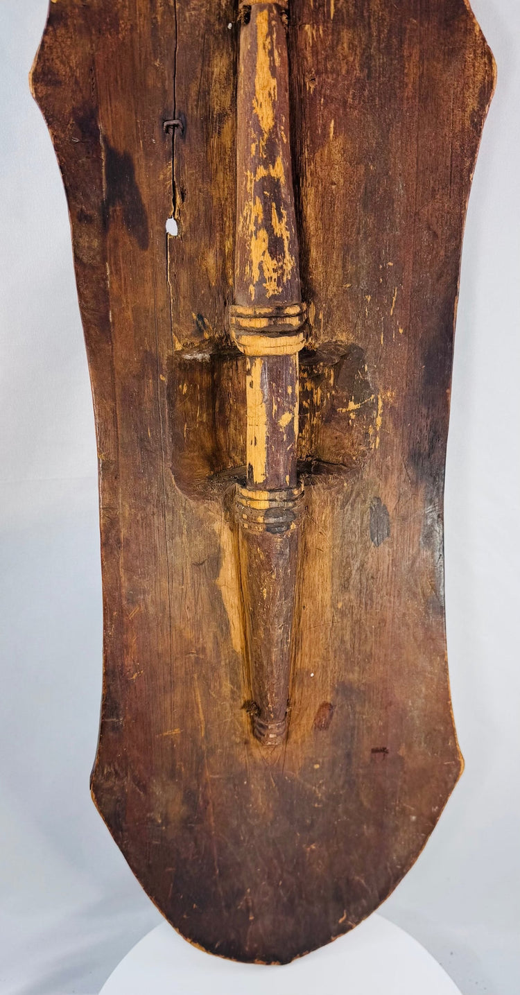 Historic cracks, surface wear, and old stabilization visible on the carved wooden shield