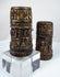 Detailed carving on a Tibetan Buddhist prayer wheel showing relief Buddha figures beneath a band of sacred inscriptions.