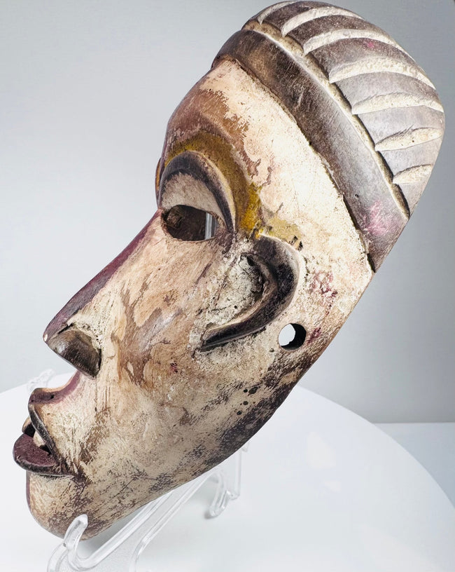 Antique African tribal mask featuring carved teeth and a deeply ridged coiffure