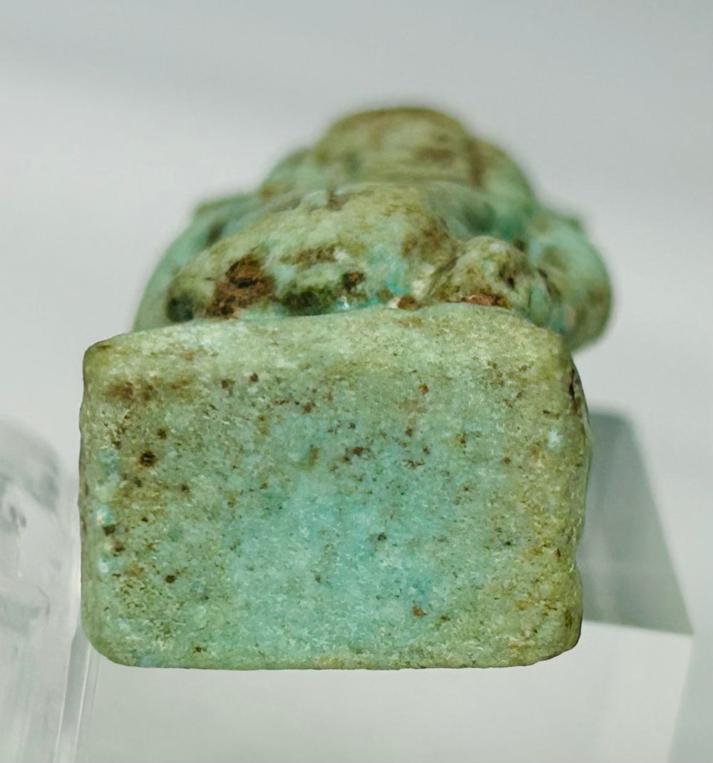 Bottom view of historic Egyptian Bes figure amulet from circa 664–332 BC photographed on neutral background