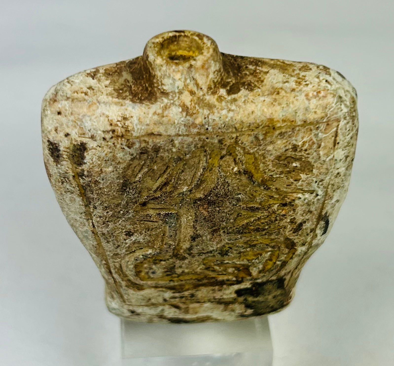 Side view of carved stone amulet flask showing natural ancient mineral deposits
