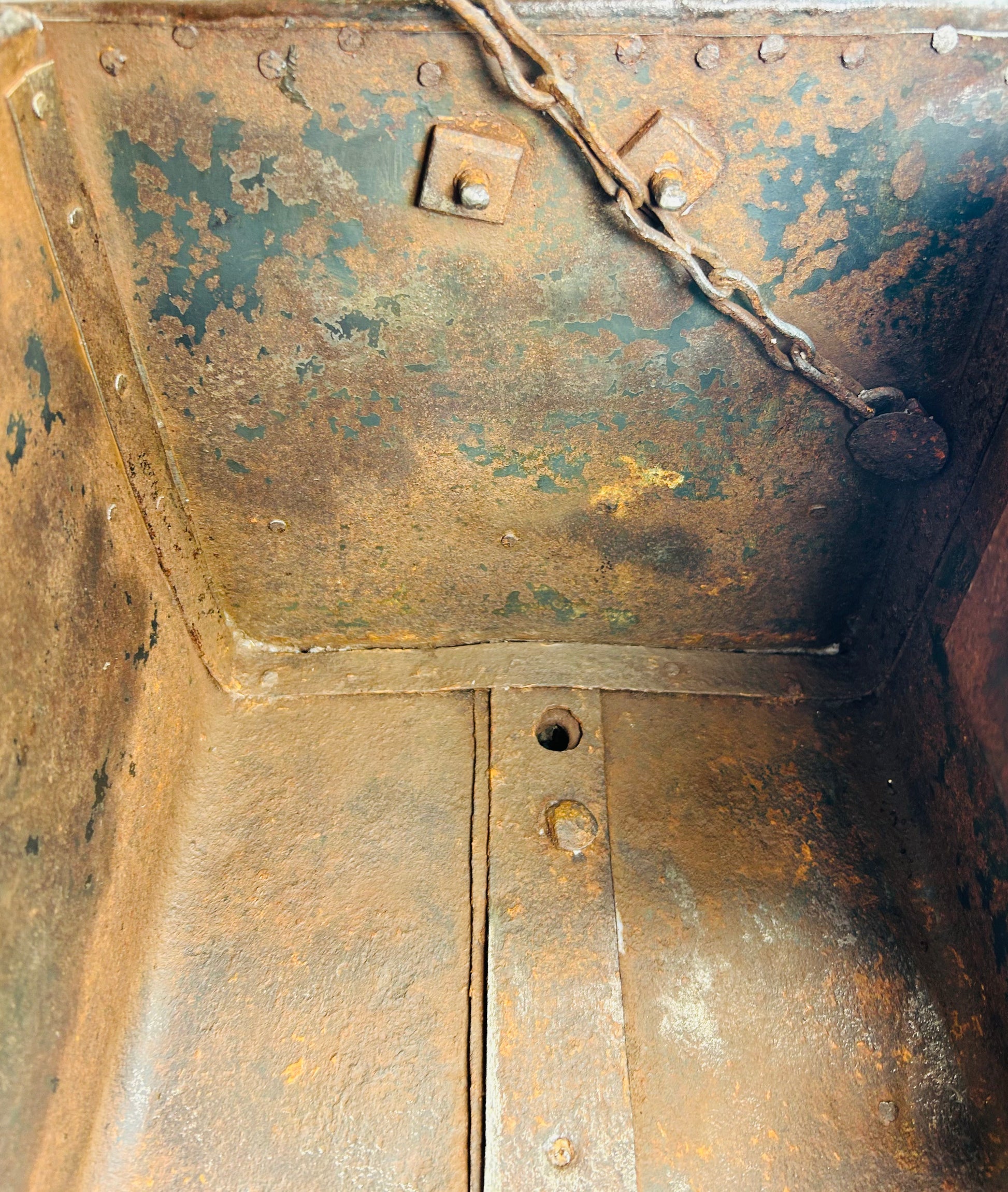 Antique iron security chest with grid-pattern strapwork, domed rivets, oxidation throughout, and functional lid and chain