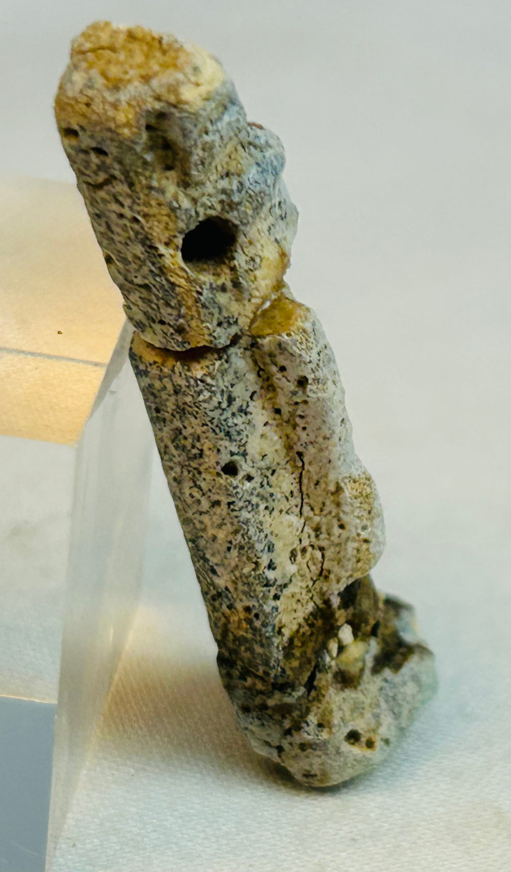 Side profile view of heavily worn faience Egyptian amulet figure with suspension hole visible.