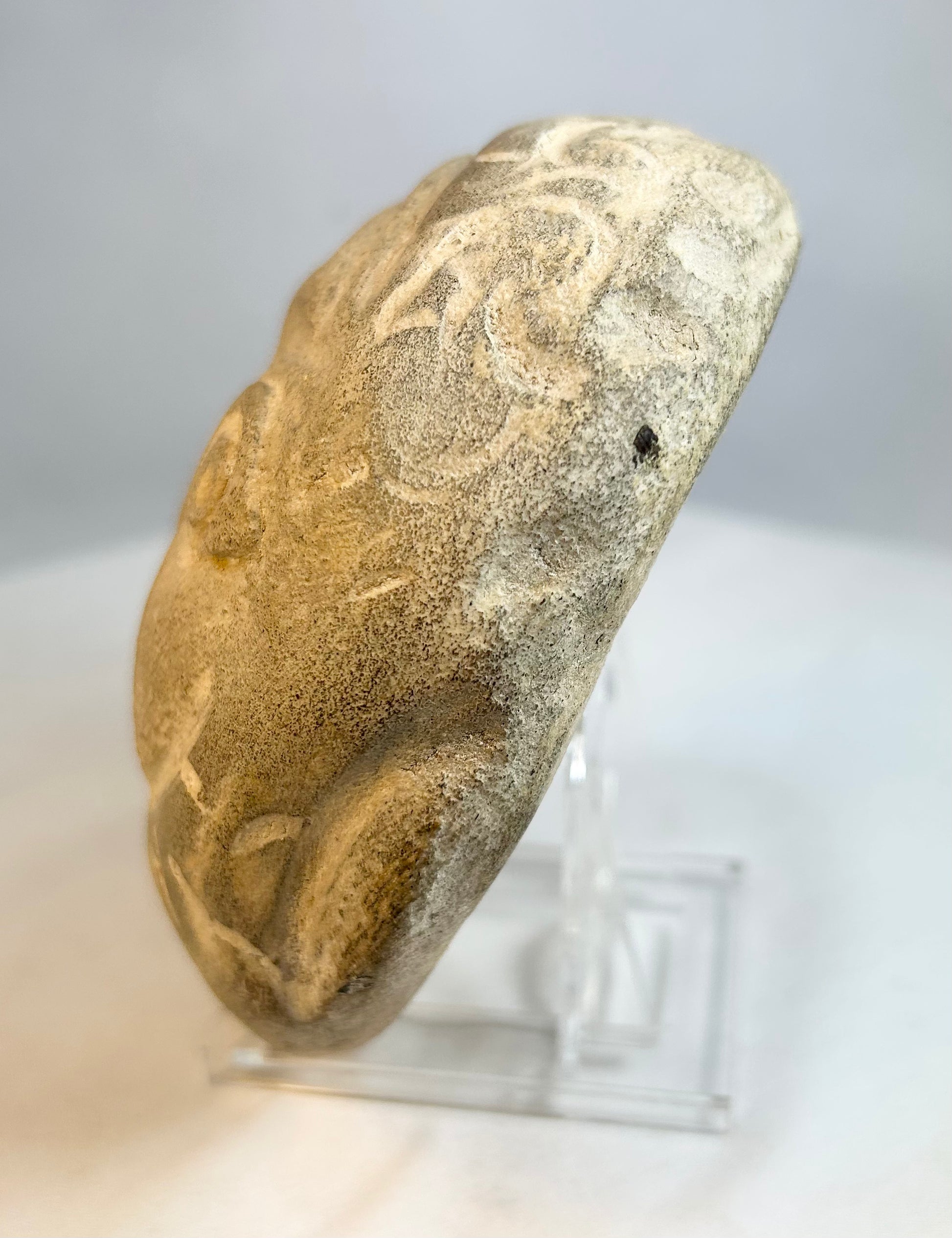 Folk art carved stone head with circular eyes and incised decorative border