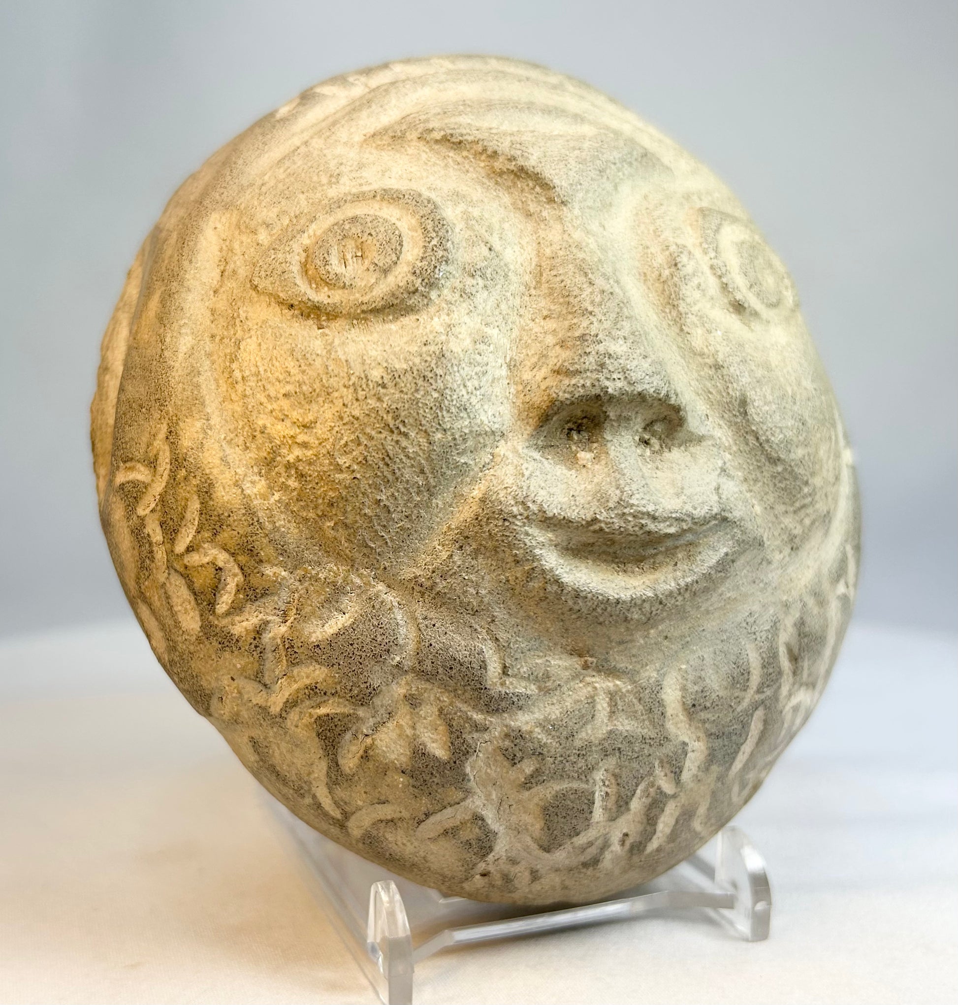 Vintage carved stone face sculpture photographed against neutral background