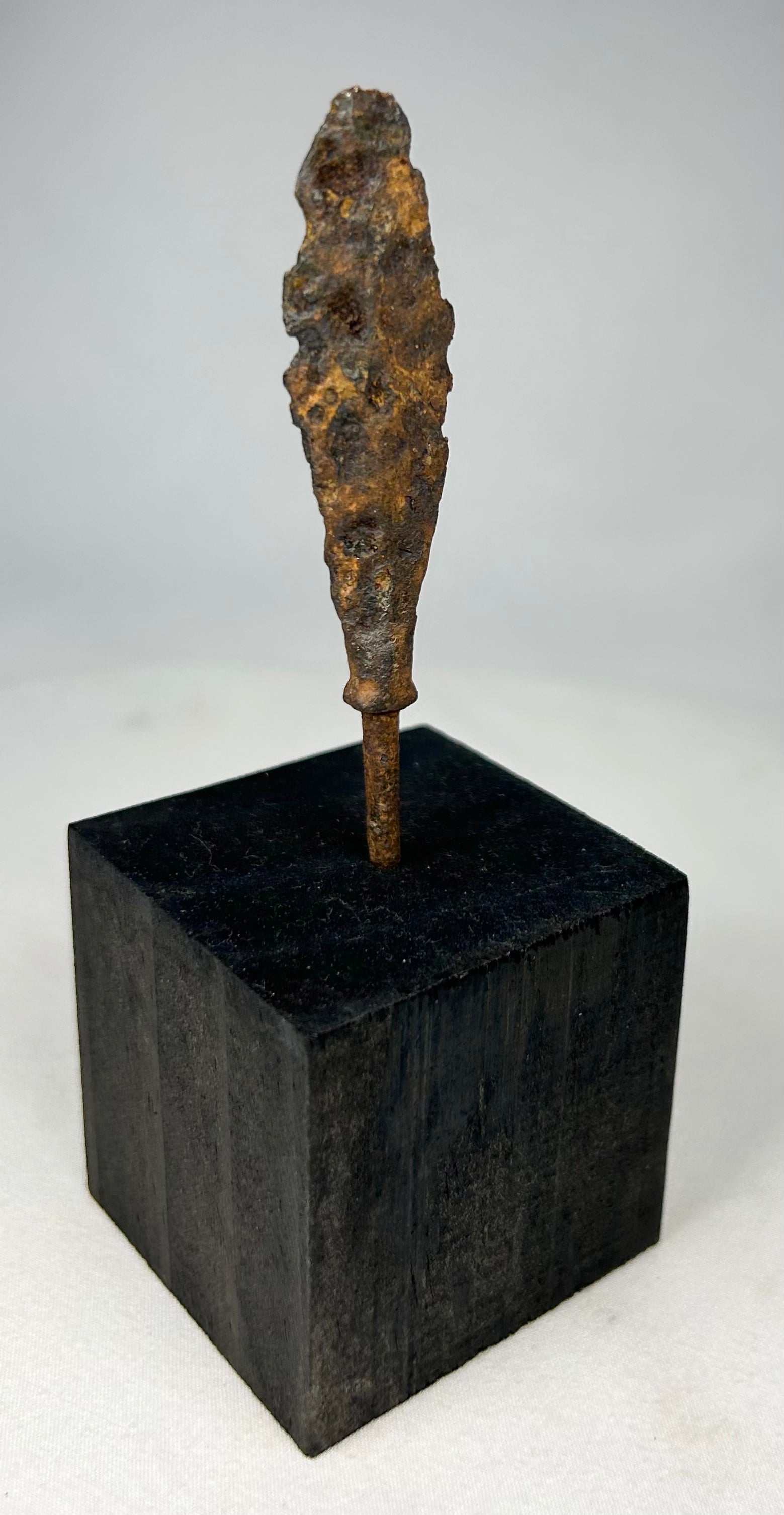 Early historic period iron arrowhead with tapered tang mounted on black wooden base