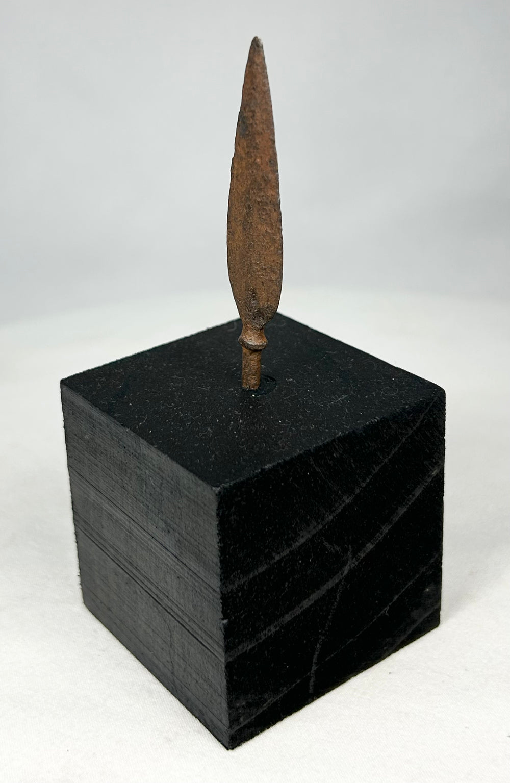 Side profile of leaf-blade iron arrowhead mounted on museum-style black stand