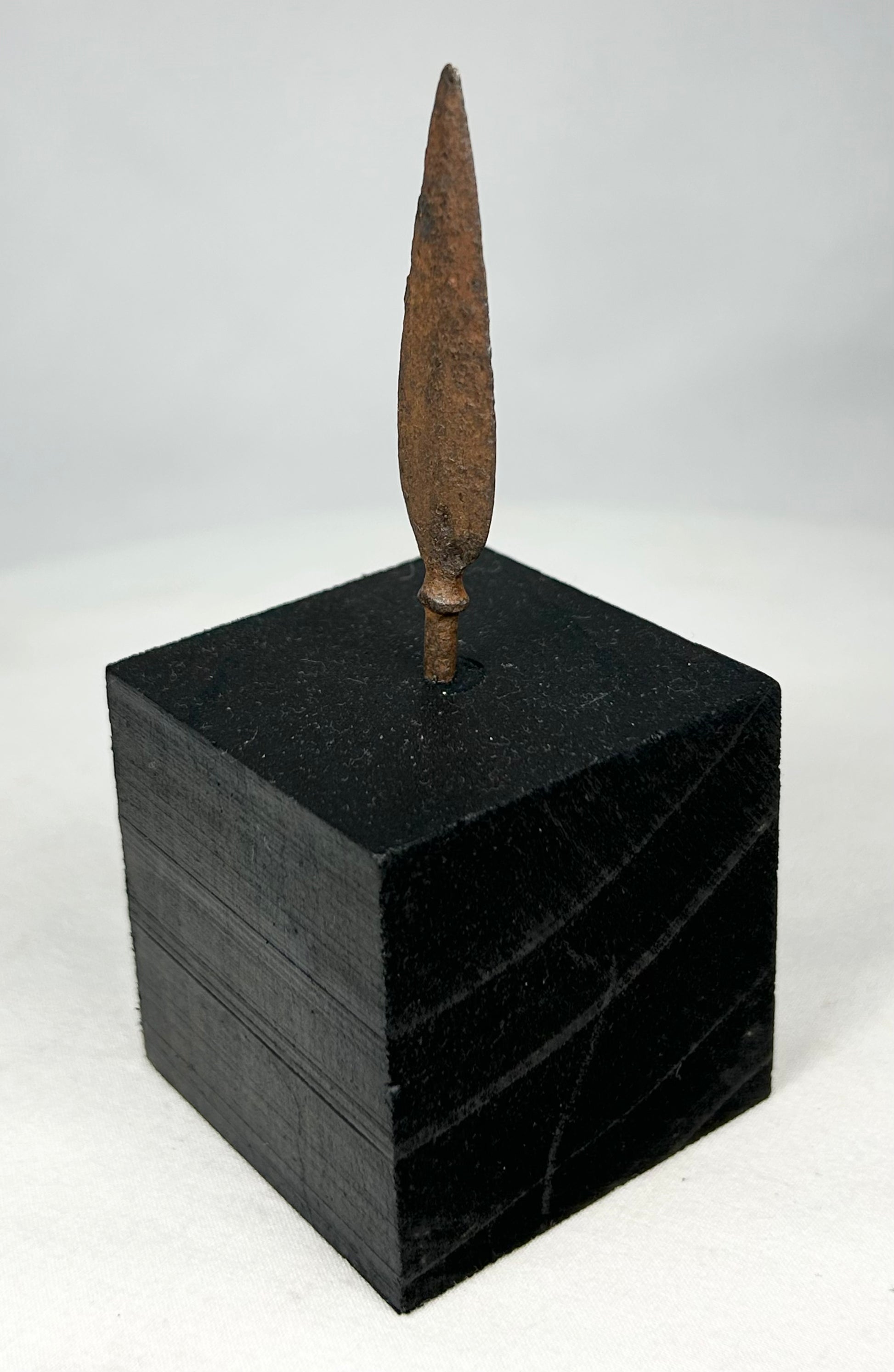 Side profile of leaf-blade iron arrowhead mounted on museum-style black stand