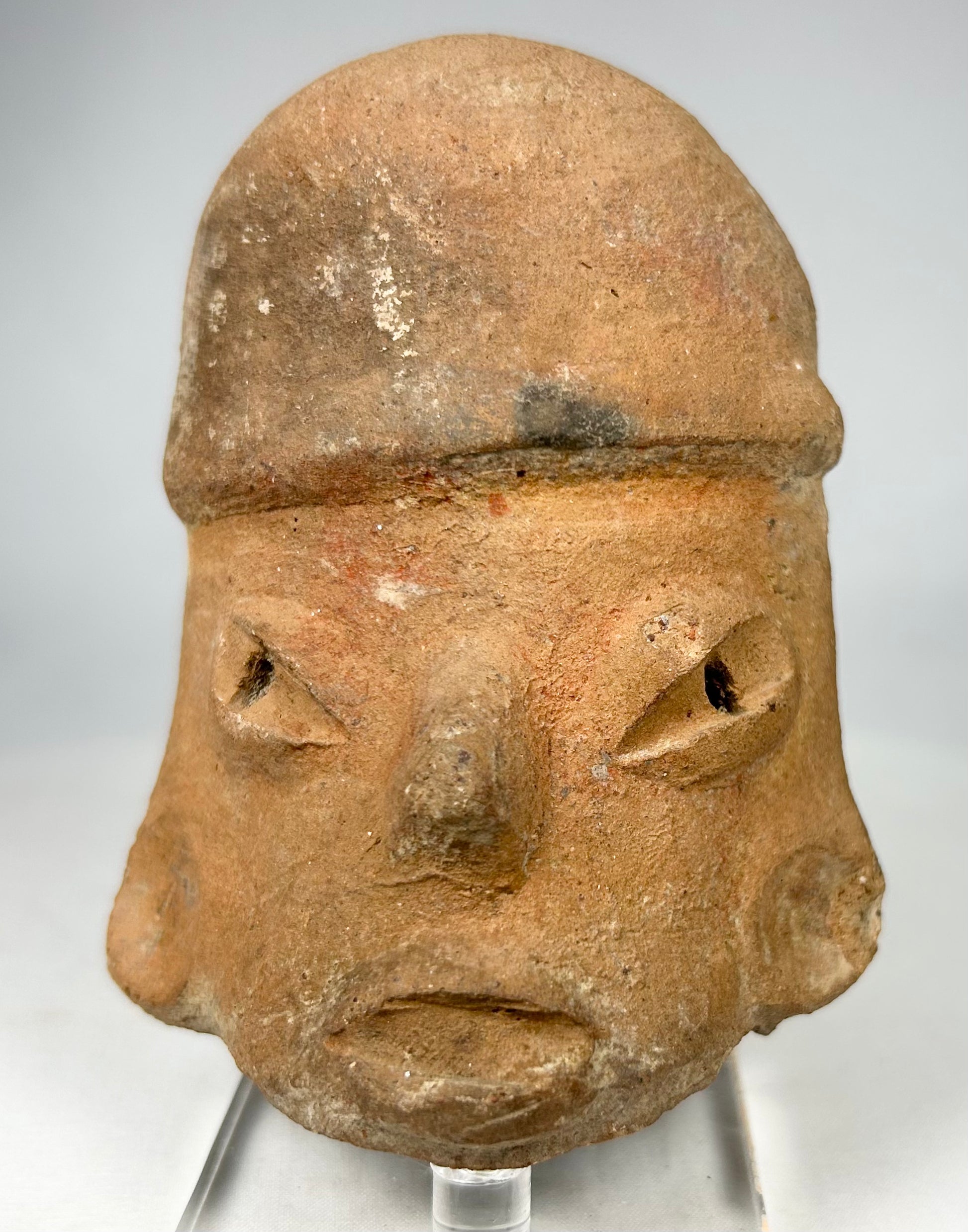 Ancient Pre-Columbian ceramic head fragment showing bold ritual facial stylization and earthen burial patina.
