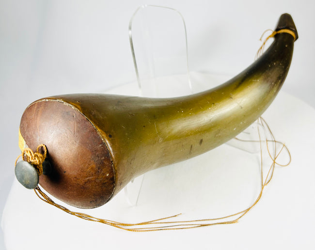 Profile view of 18th–19th century horn powder vessel with rich amber tones