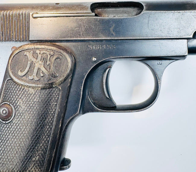 Browning Model 1906 showing its oval FN grip emblem, slotted grip screw, checkered grip panel, and ejection port.