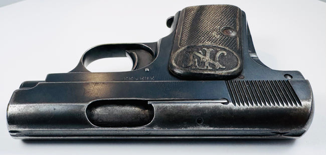 FN Browning Model 1906 with a narrow steel slide, oval ejection port, and textured grip bearing the FN emblem.