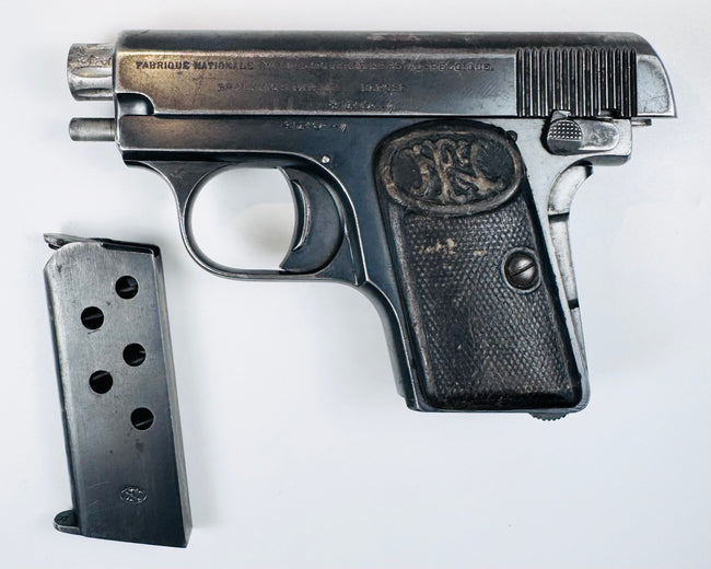 Deactivated FN Browning Model 1906 with its slide held open and a detached steel magazine displayed beside it.