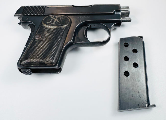 Browning Model 1906 pocket pistol beside a detached metal magazine with circular inspection holes.