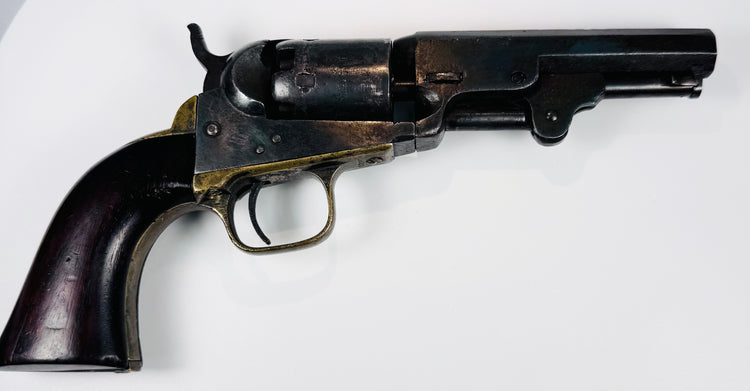 Antique Colt Model 1849 Pocket Revolver with an exposed hammer, worn steel cylinder, and warm-toned brass trigger guard.
