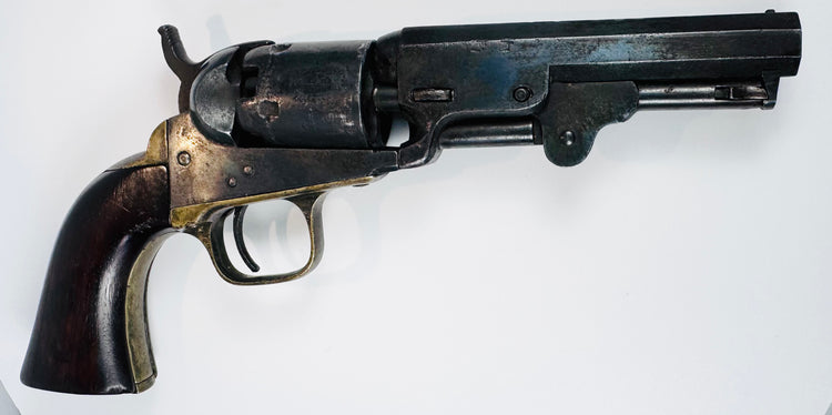 Colt Model 1849 Pocket Revolver with its loading lever folded beneath the barrel and brass fittings bordering the walnut grip.
