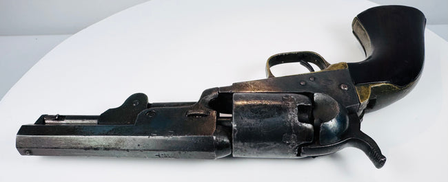 Colt Model 1849 Pocket Revolver highlighting the octagonal barrel, cylinder contours, and curved walnut grip against a white background.