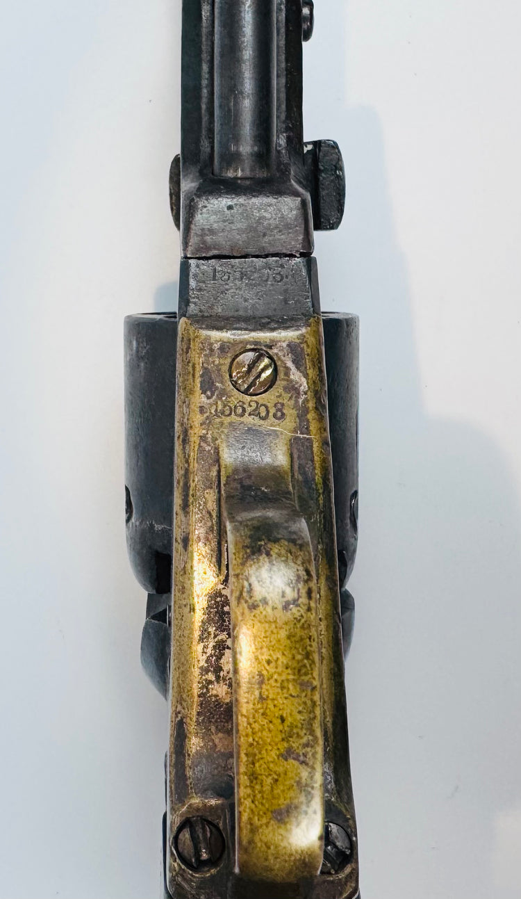 Close-up of the Colt Model 1849 Pocket Revolver’s brass grip frame, with screws, worn markings, and aged patina.
