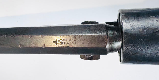 Close-up of faint stamped lettering and surface wear on the Colt Model 1849 Pocket Revolver’s octagonal steel barrel.