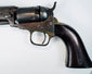 Colt Model 1849 Pocket Revolver detail showing the cylinder and exposed hammer above the brass trigger guard and walnut grip.