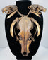 Skull and tooth necklace displayed on a black bust, with pale curved teeth framing the elongated central skull.