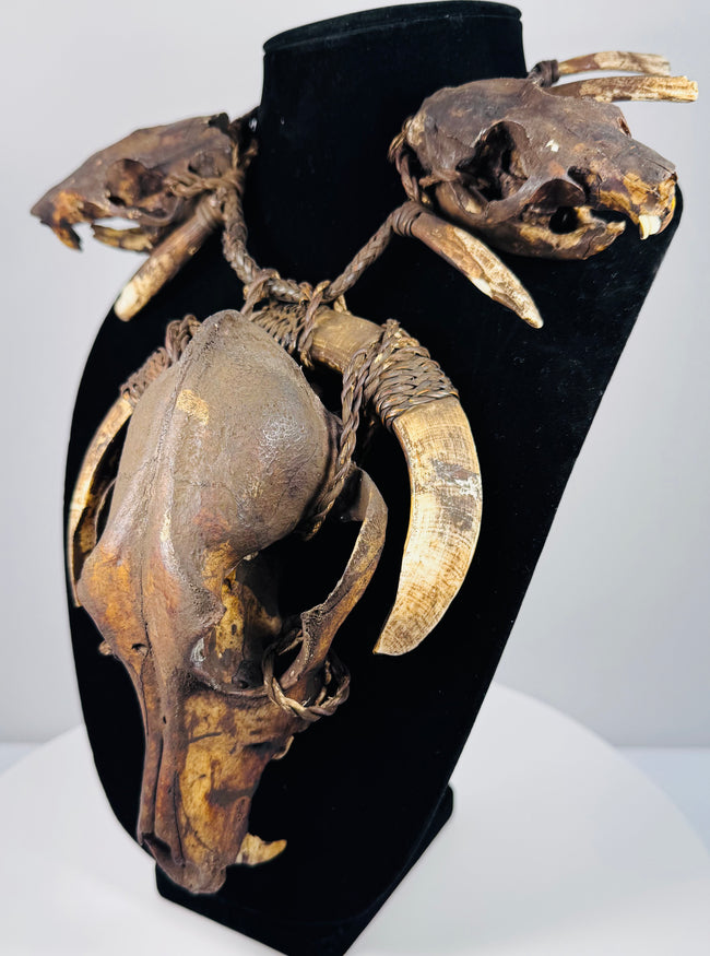 Animal skull necklace highlighting the central skull’s elongated muzzle, open eye socket, and surrounding twine bindings.