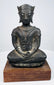 Bronze Buddha statue with a calm expression, winged crown ornaments, and lighter surface wear across its dark patina.