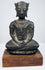 Seated bronze Buddha displaying raised chest decoration, rounded shoulders, and folded hands above crossed legs.