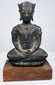 Seated bronze Buddha displaying raised chest decoration, rounded shoulders, and folded hands above crossed legs.