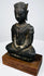 Crowned bronze Buddha with textured metal surfaces and an oval bronze seat mounted on a rectangular wooden base.