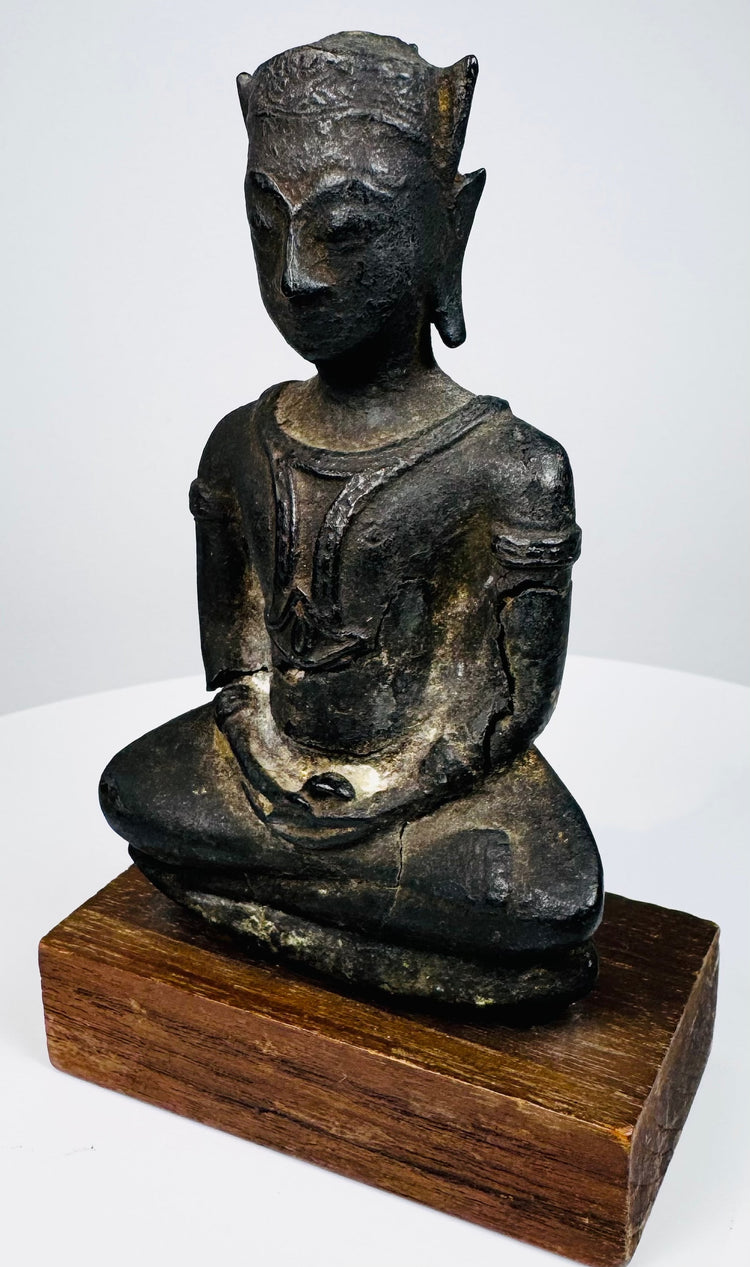 Crowned bronze Buddha with textured metal surfaces and an oval bronze seat mounted on a rectangular wooden base.