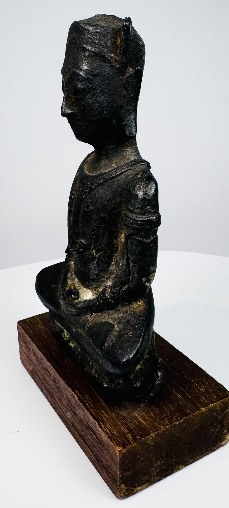 Bronze Buddha highlighting elongated ear ornaments, a slender torso, and crossed legs resting on a low bronze plinth.
