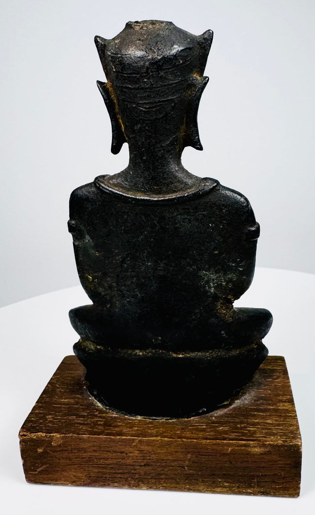 Crowned bronze Buddha with an upright seated posture, a rounded bronze seat, and a warm brown wooden display base.