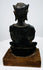Crowned bronze Buddha with an upright seated posture, a rounded bronze seat, and a warm brown wooden display base.