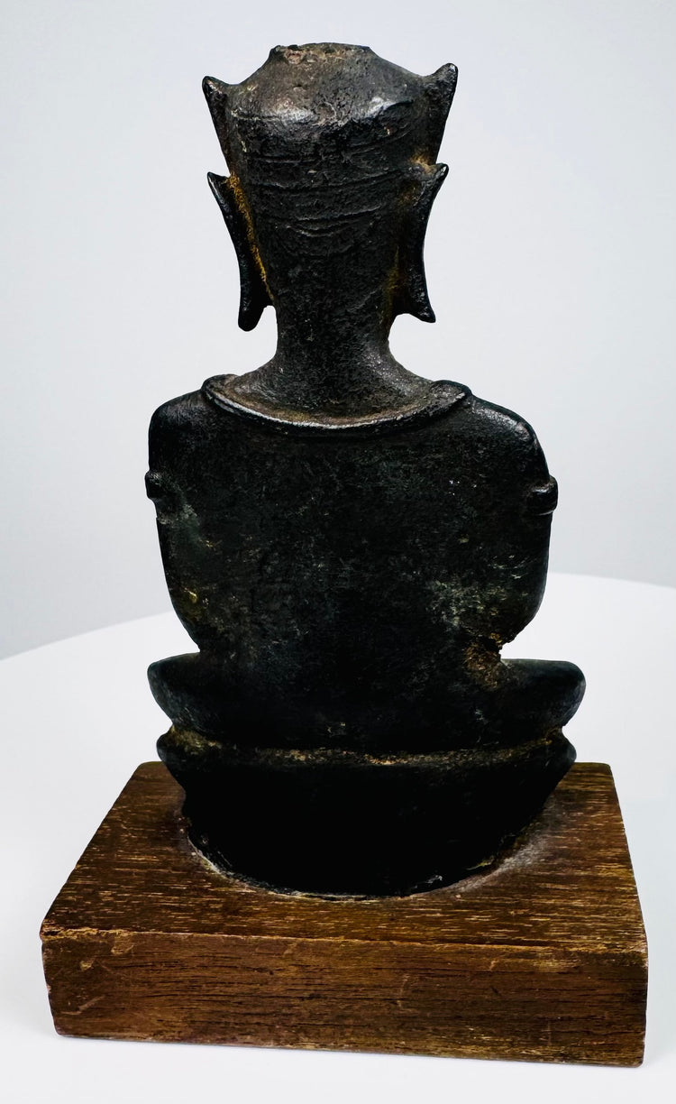 Crowned bronze Buddha with an upright seated posture, a rounded bronze seat, and a warm brown wooden display base.
